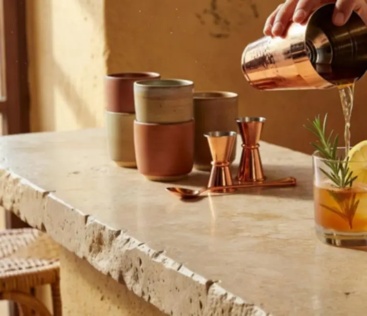 Main d’un barman dressant un cocktail maison avec agrumes et herbes fraîches sur un comptoir en pierre.